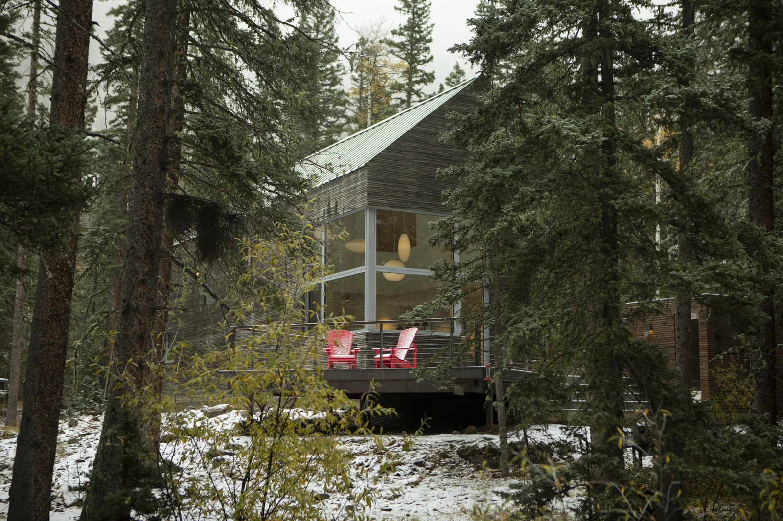 9k House among the pines after early snow, its glazed corner lit from within