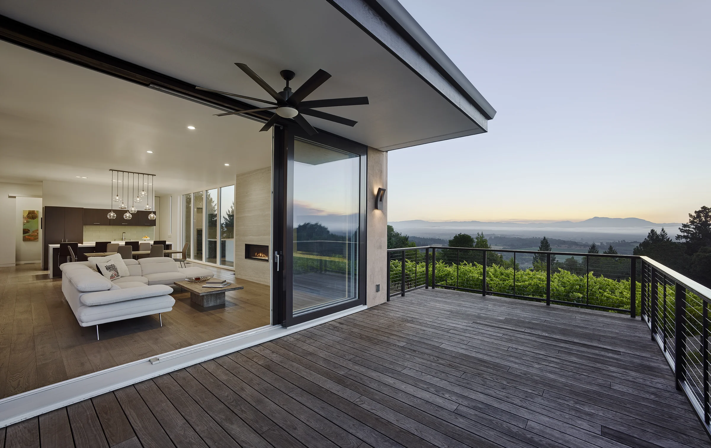 The deck at Forestville Residence at dusk, a lift-slide door pushed open to the living room with the valley beyond