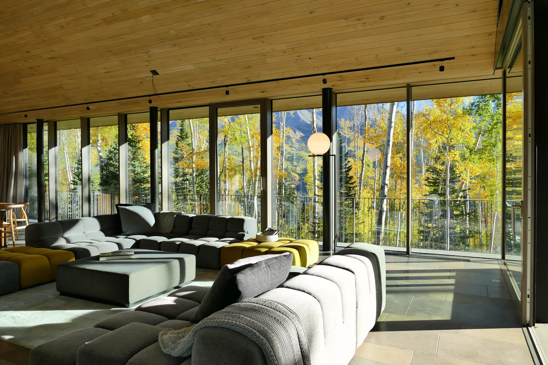 Clad wood glazing along the living room at Highlands Way, opening to autumn aspens and the peaks beyond