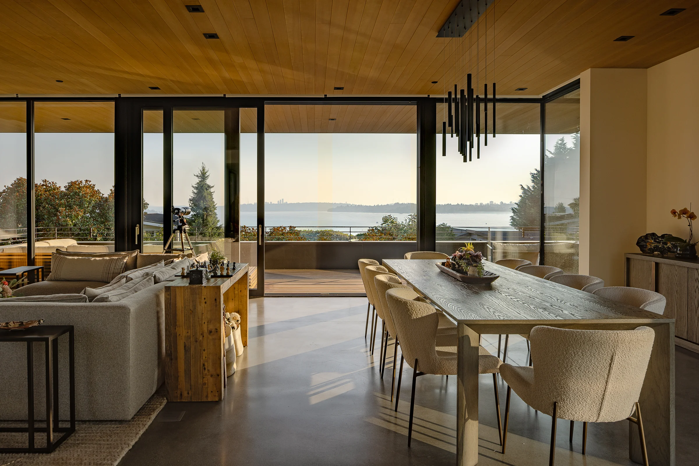 Aluminum sliding walls opening a Westward House living and dining room to Puget Sound at dusk